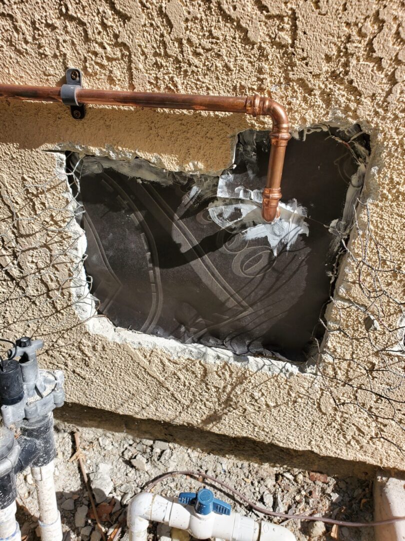 A hole in the wall with copper pipes and wires.