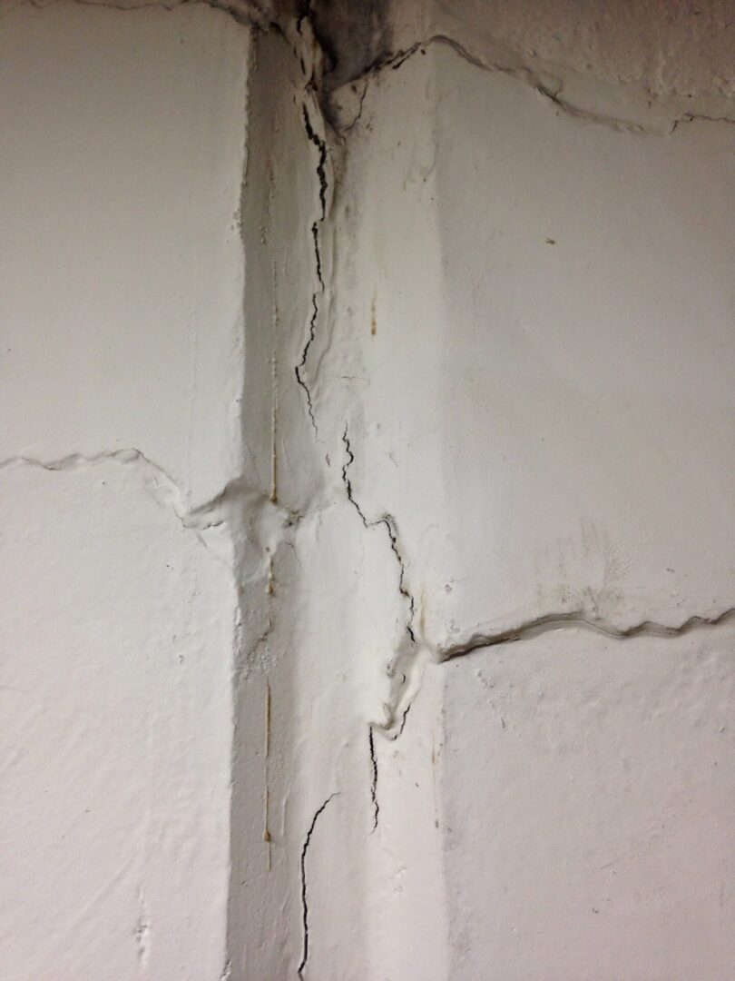 A wall with cracks in it and the corner of the room.