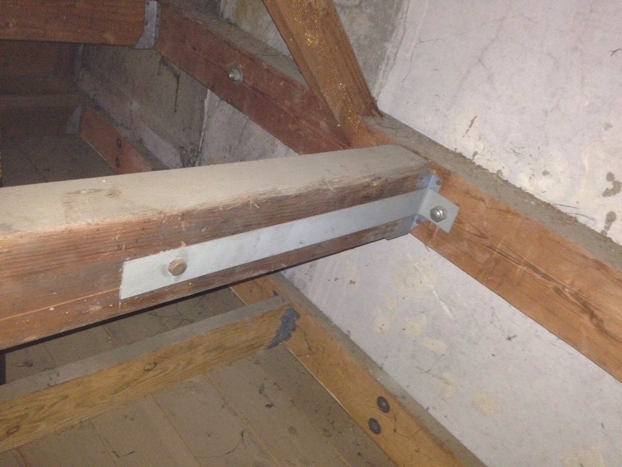 A wooden beam with metal support bars in the middle of an attic.