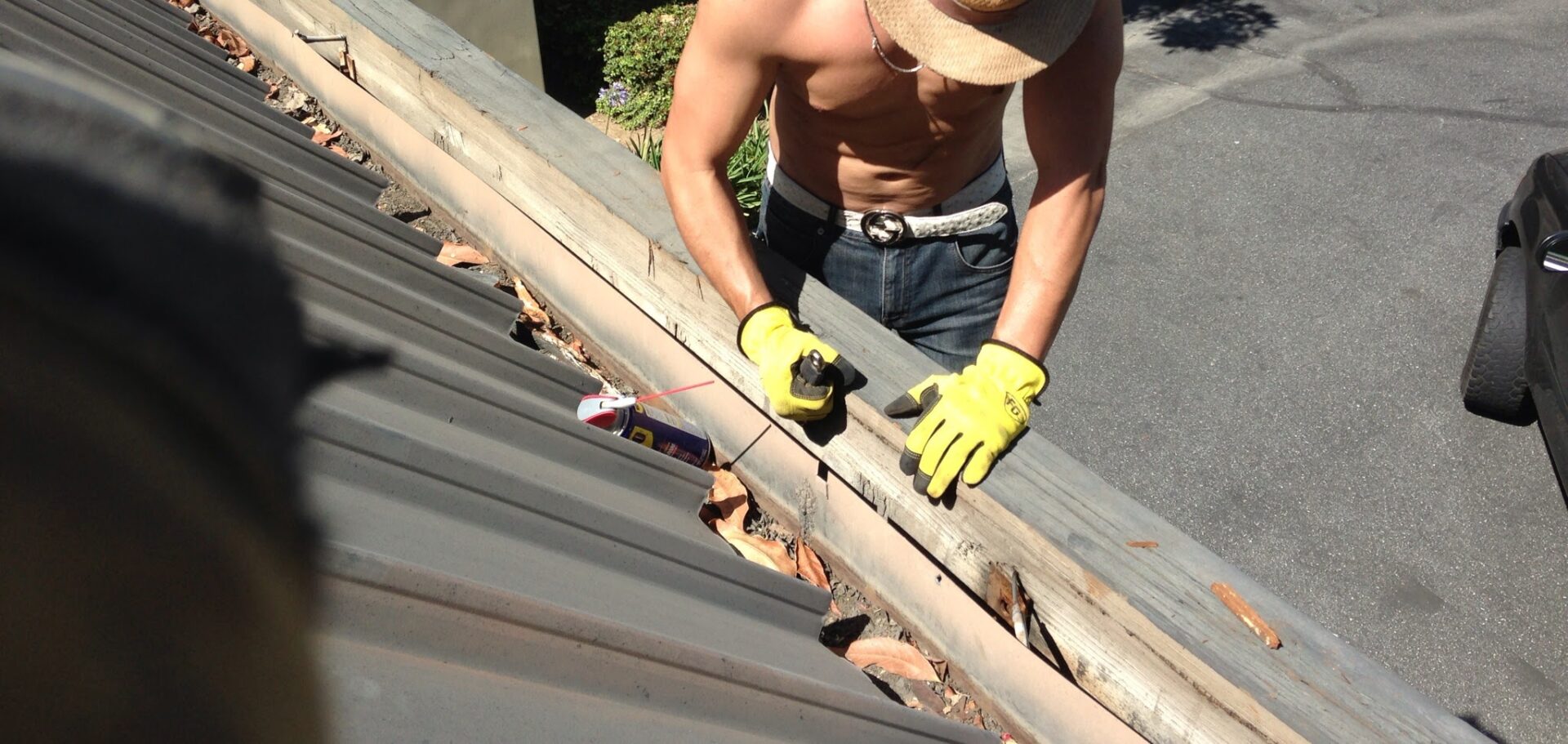 A man in yellow gloves working on the roof of his house.