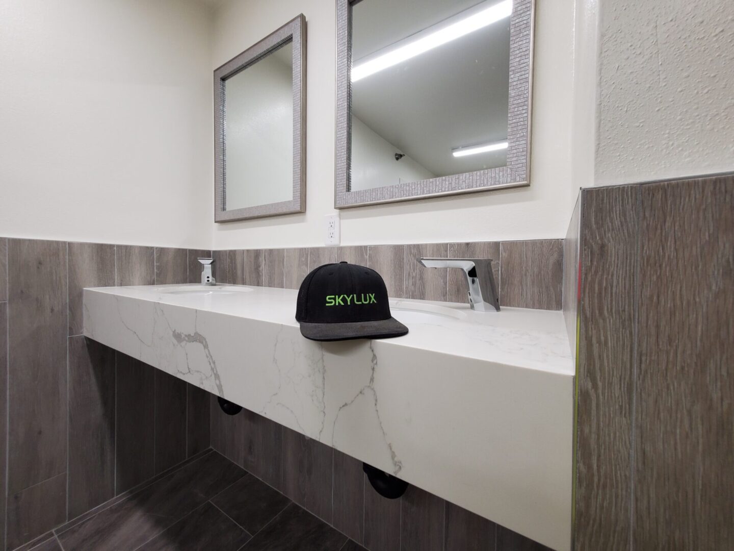 A bathroom with two sinks and mirrors, one of which has a hat on it.